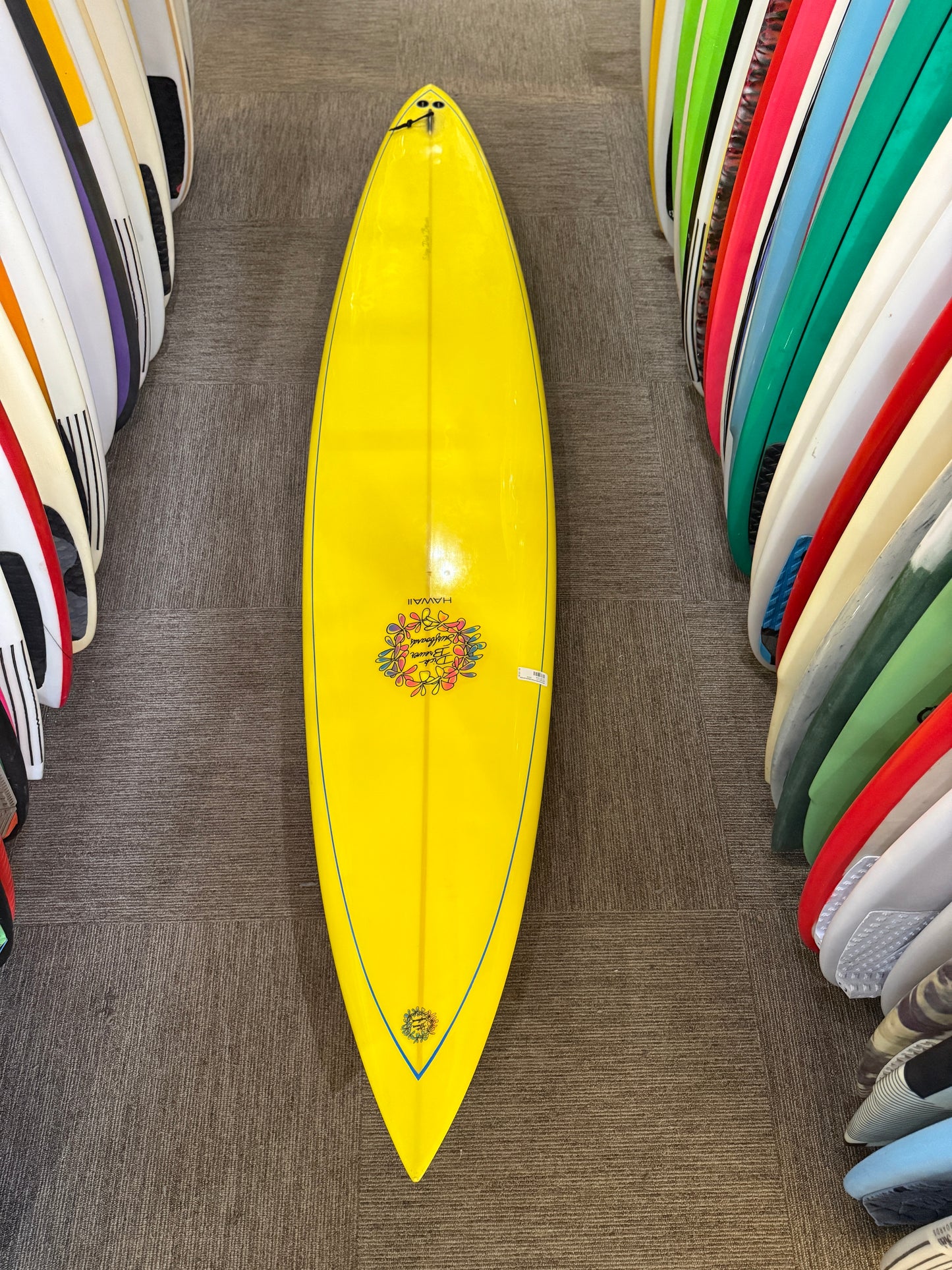 Yellow surfboard with a logo on a wooden floor surrounded by other colorful surfboards.